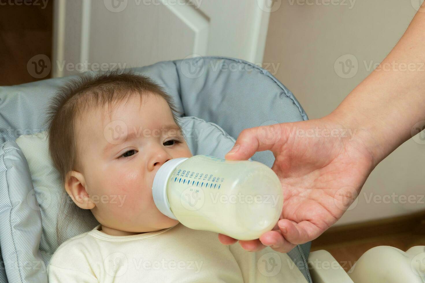 bebê menina em uma alimentando cadeira ser alimentado Fórmula a partir de uma garrafa foto