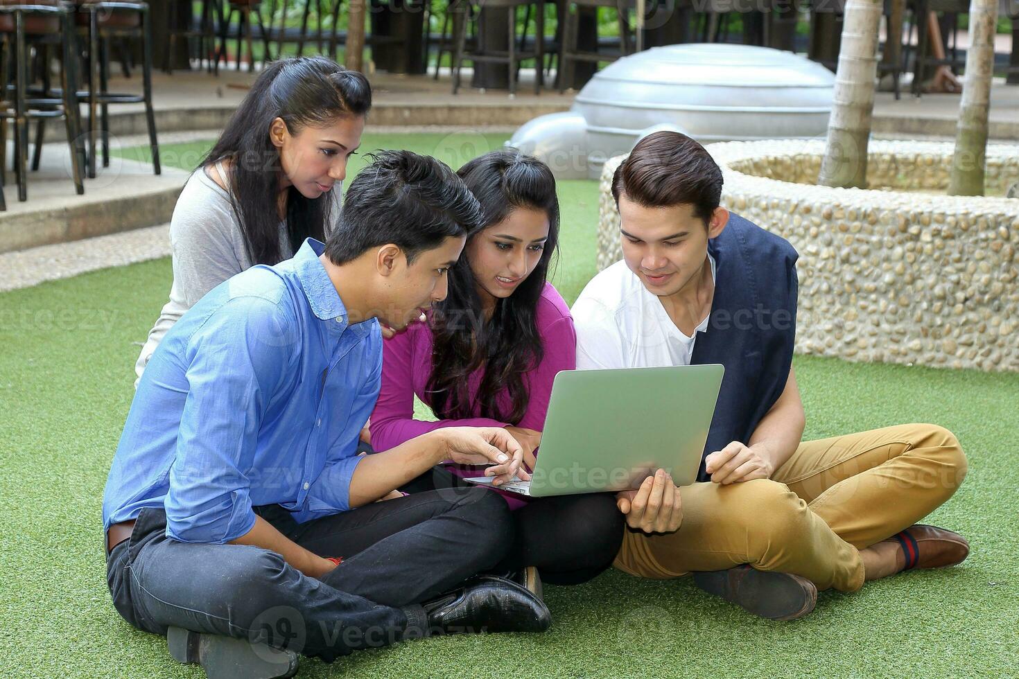 grupo do ásia jovem homem mulher amigo aluna colegas picada em verde Relva conversa misturar-se discutir estude computador computador portátil foto