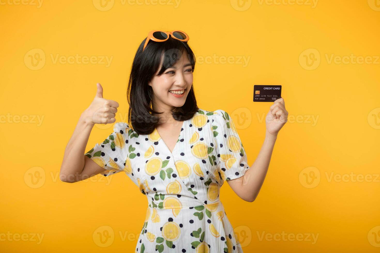 retrato jovem ásia mulher feliz sorridente dentro primavera vestir mostrando plástico crédito cartão isolado em amarelo fundo. pagar, dinheiro e compra compras Forma de pagamento conceito. foto