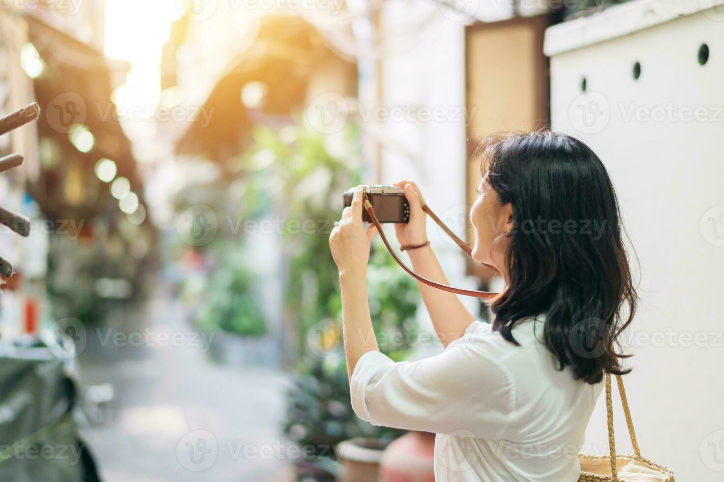 feliz juventude ásia mulher pessoa com Câmera viaja rua cidade viagem em lazer fim de semana. jovem hipster menina fêmea turista passeios turísticos verão urbano Bangkok destino estilo de vida conceito. foto