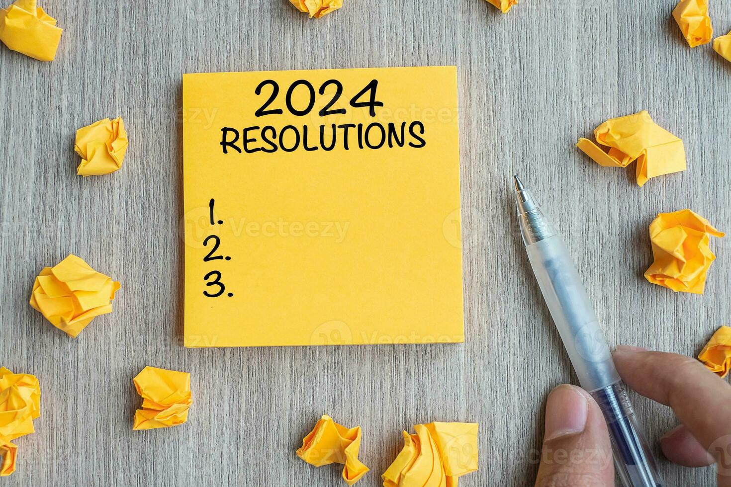 2024 resoluções palavra em amarelo Nota com homem de negocios segurando caneta e desintegrado papel em de madeira mesa fundo. Novo ano começar, estratégia e objetivo conceito foto