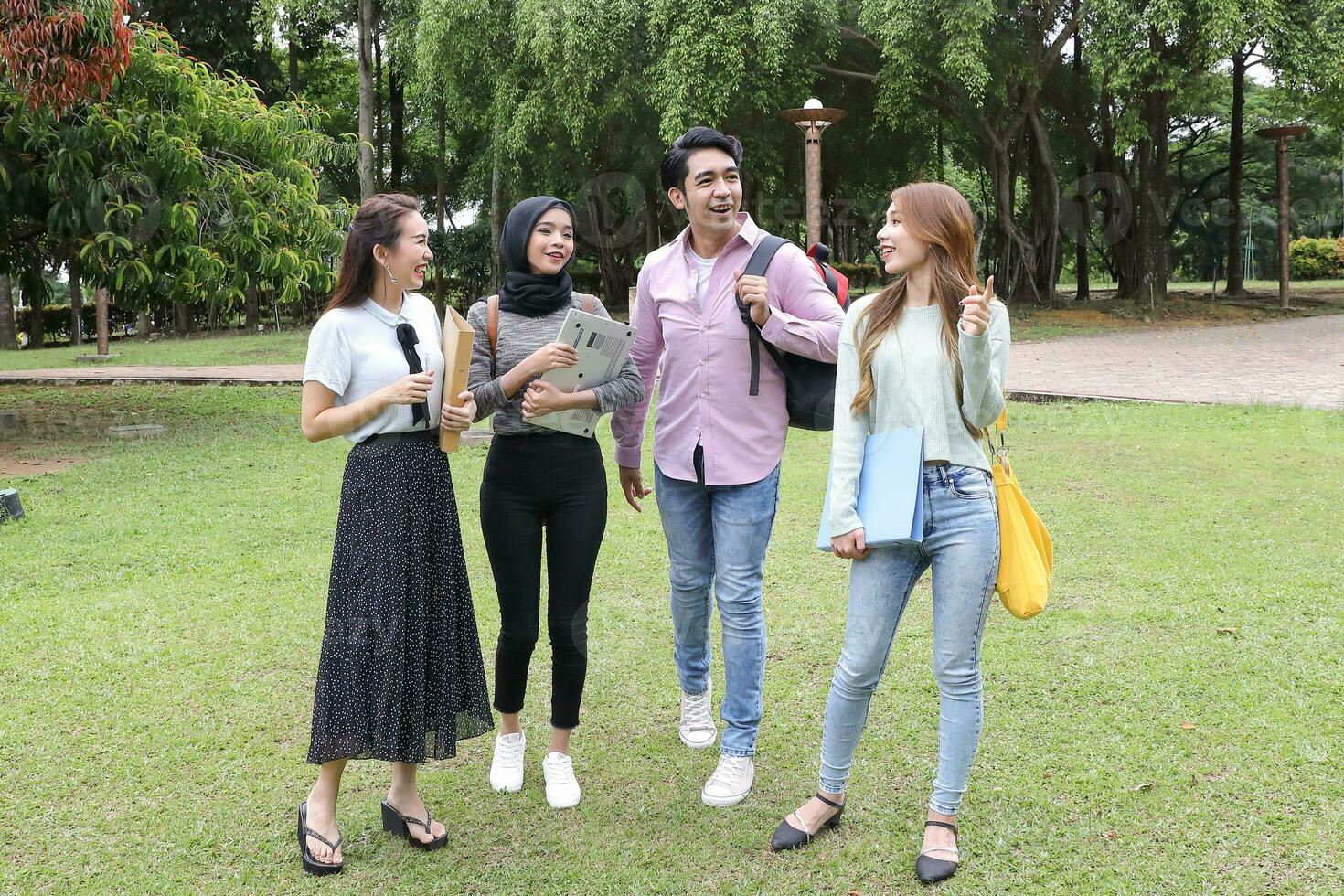 jovem ásia malaio chinês homem mulher ao ar livre parque andar ficar de pé estude conversa discutir ponto computador portátil Arquivo livro mochila foto