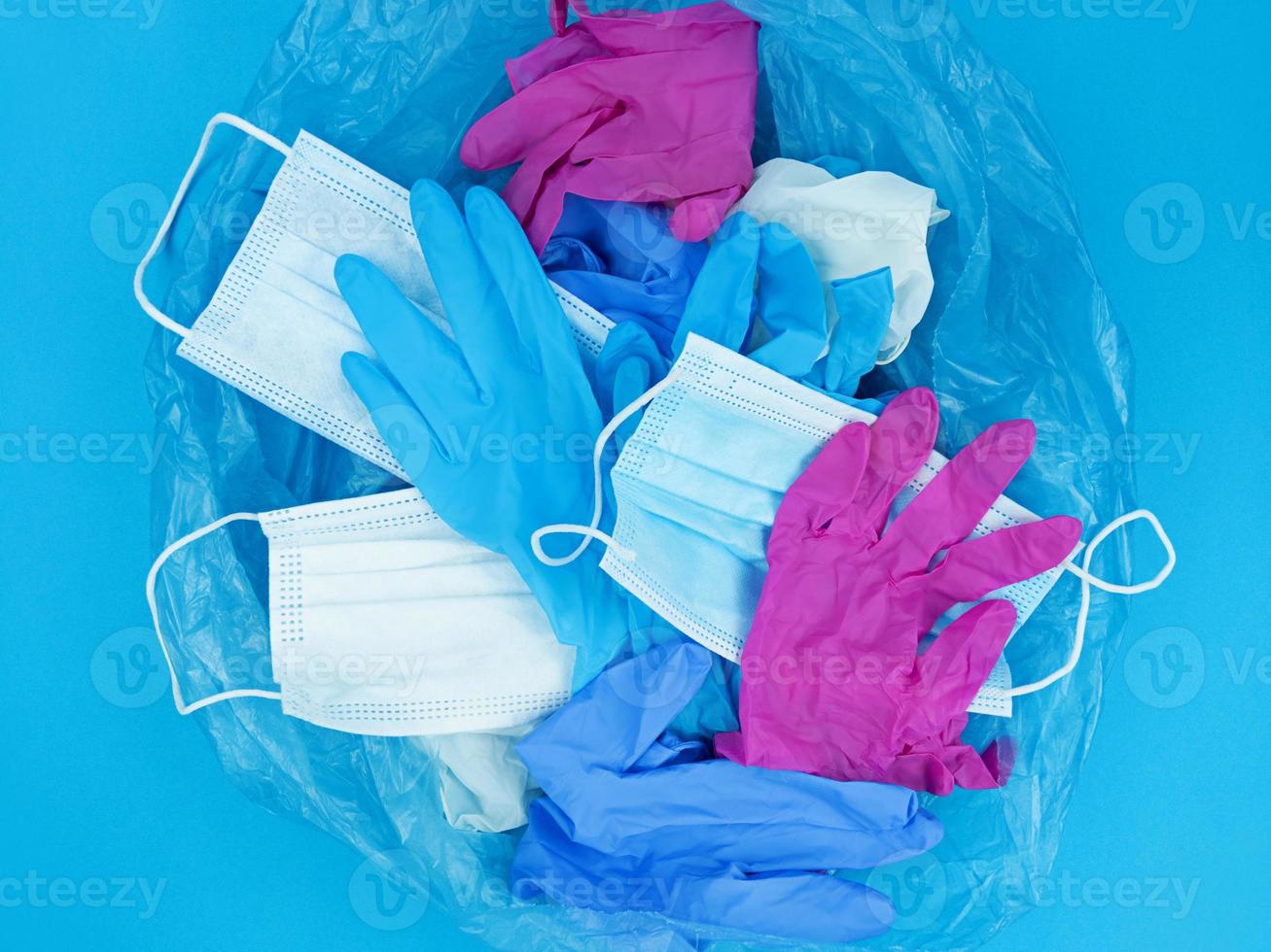 Máscaras faciais para resíduos de coronavírus pandêmico médico e luvas de látex em um saco de lixo sobre fundo azul foto