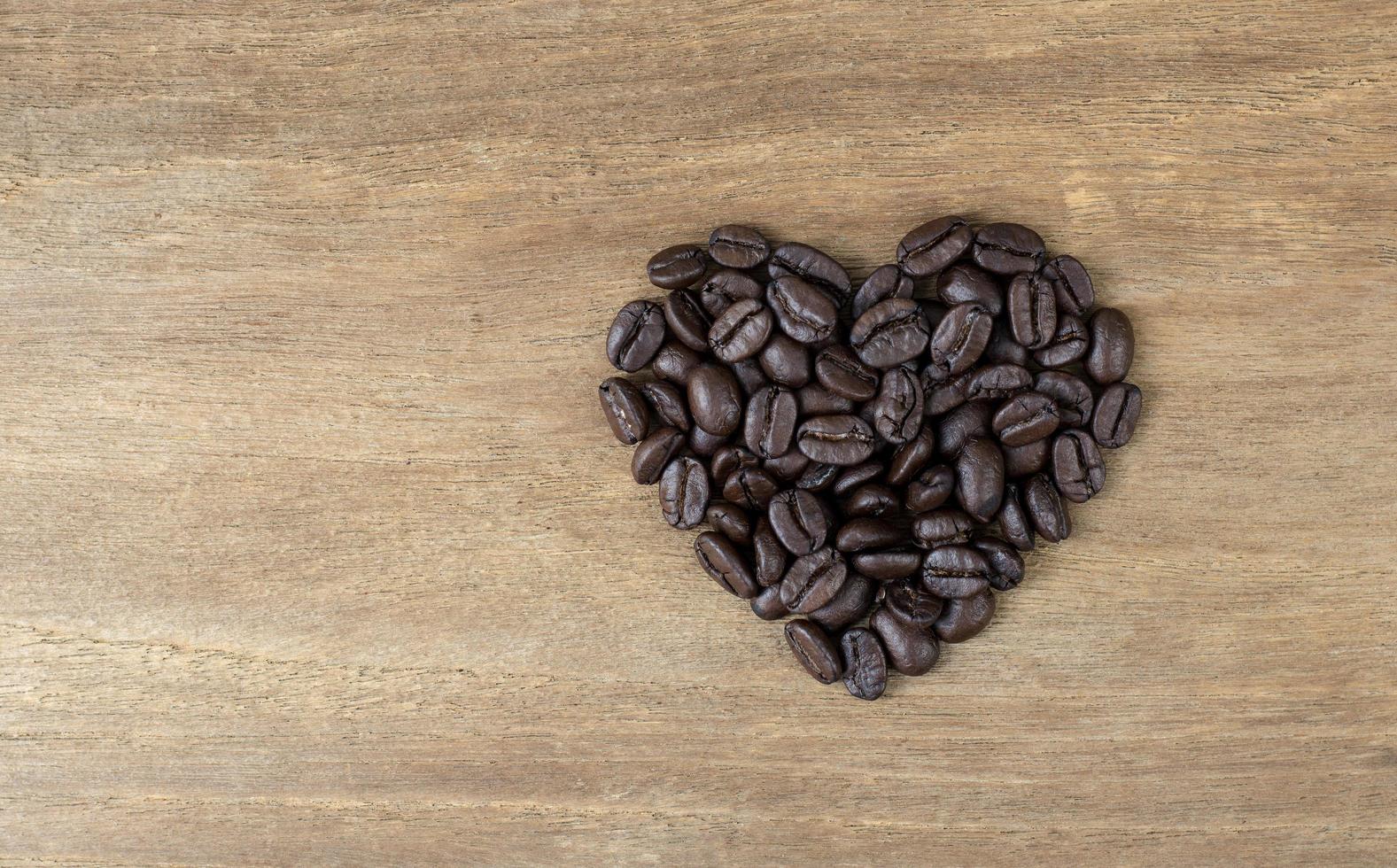 grãos de café em forma de coração em fundo de madeira foto