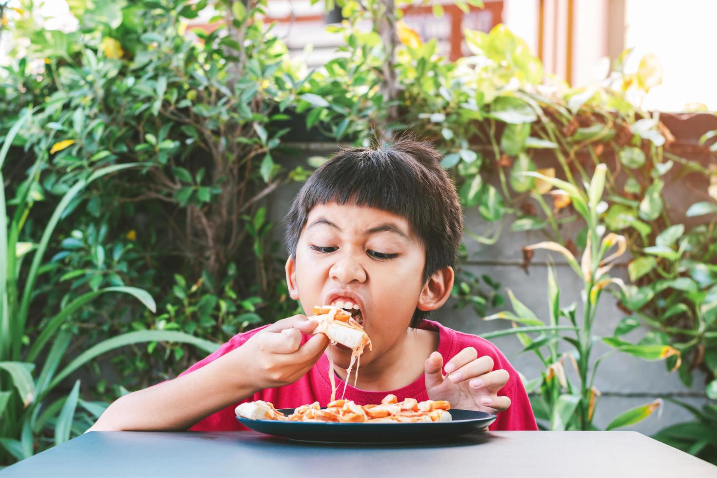 menino asiático fofo sentado feliz comendo pizza foto