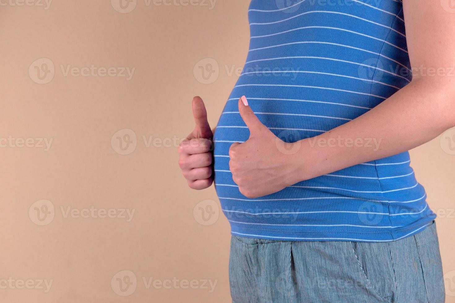 uma visão de perto da barriga de uma mulher grávida em um azul mostra um sinal de semelhante foto