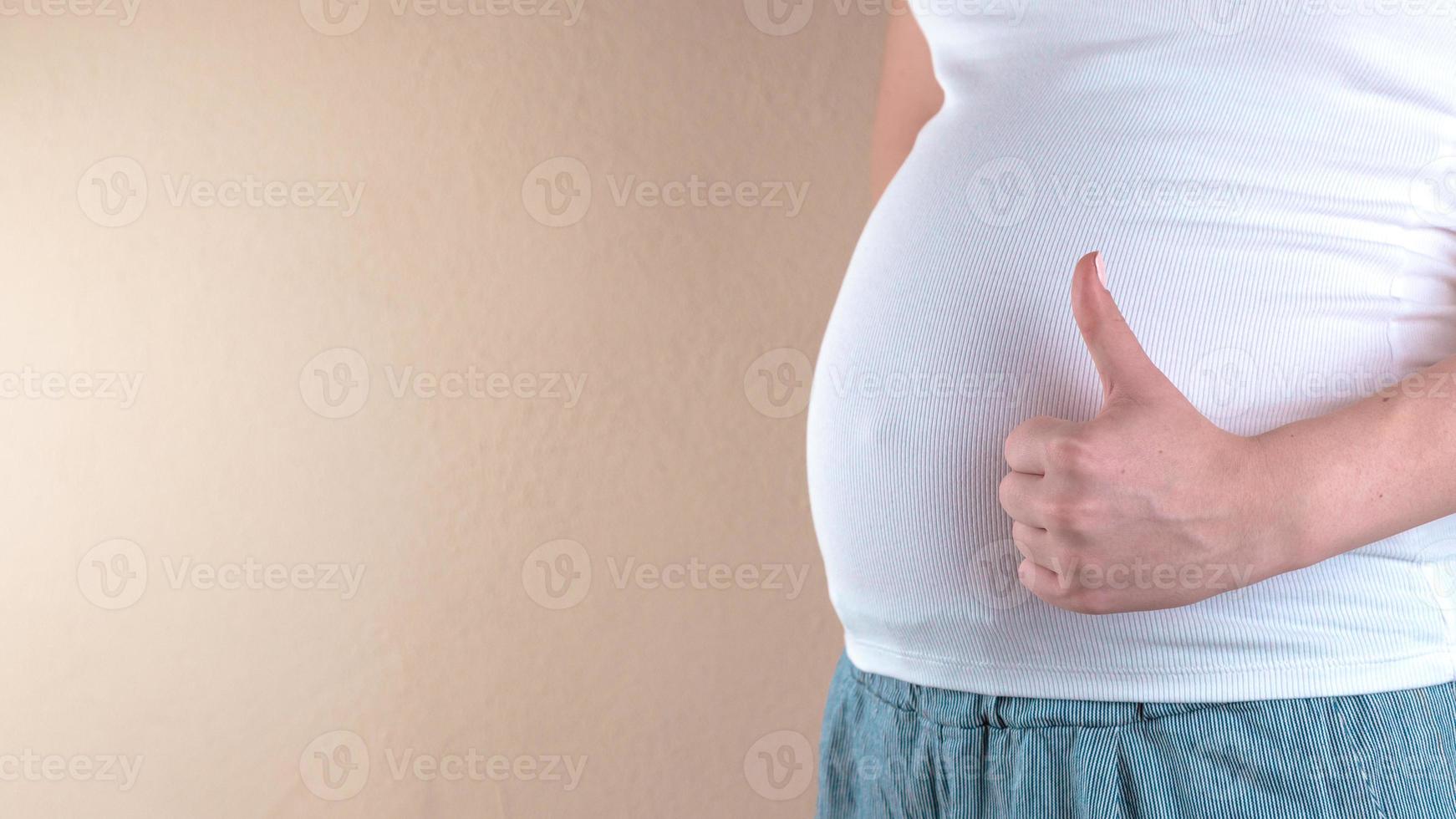 uma visão em close-up da barriga de uma mulher grávida em uma camiseta branca que mostra um sinal de semelhante foto