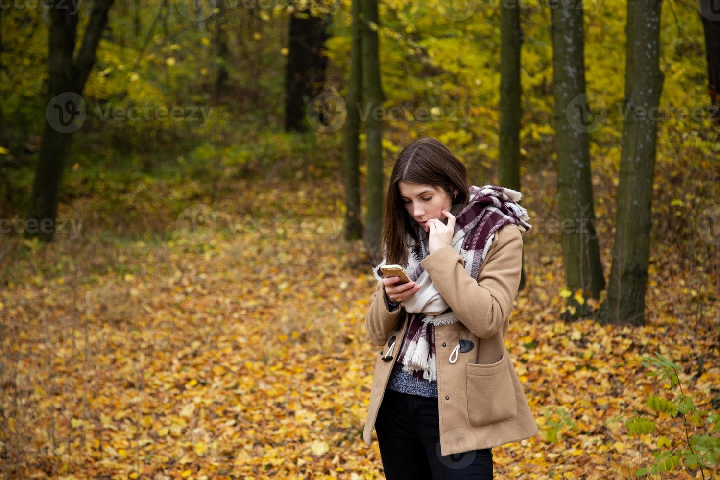 linda garota com uma jaqueta marrom na floresta de outono foto