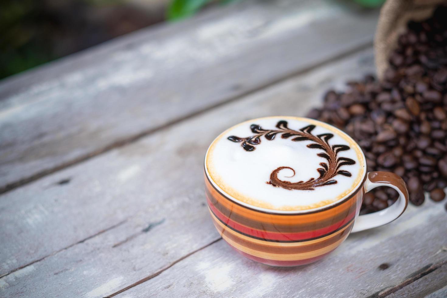 café cappuccino quente na velha mesa de madeira com grãos de café torrados foto