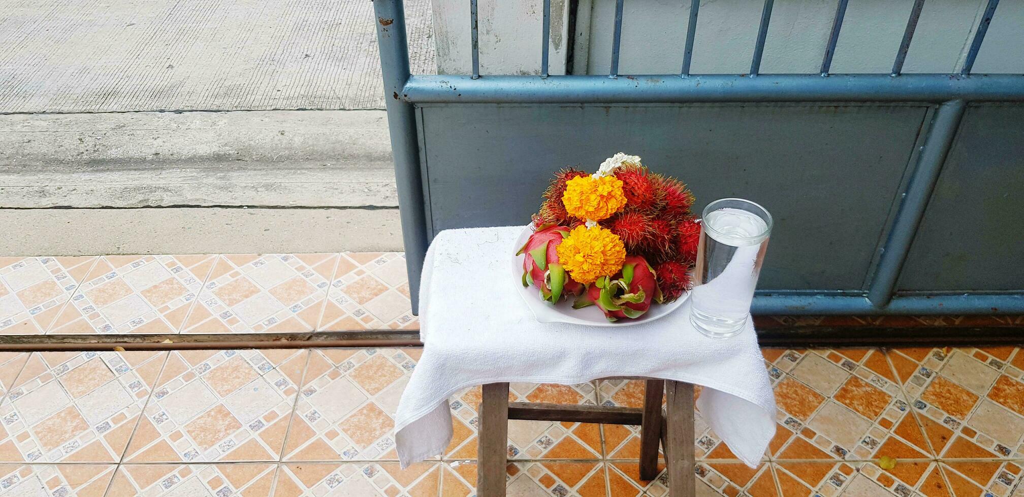 fresco festão flor com rambutã, Dragão fruta e vidro do água em mesa com azul inoxidável aço cerca e colorida telha fundo com cópia de espaço foto