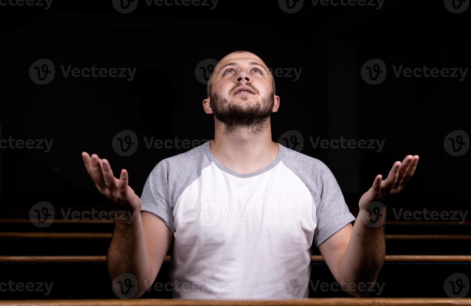 um homem cristão de camisa branca está sentado com as mãos para cima e orando com o coração humilde na igreja foto