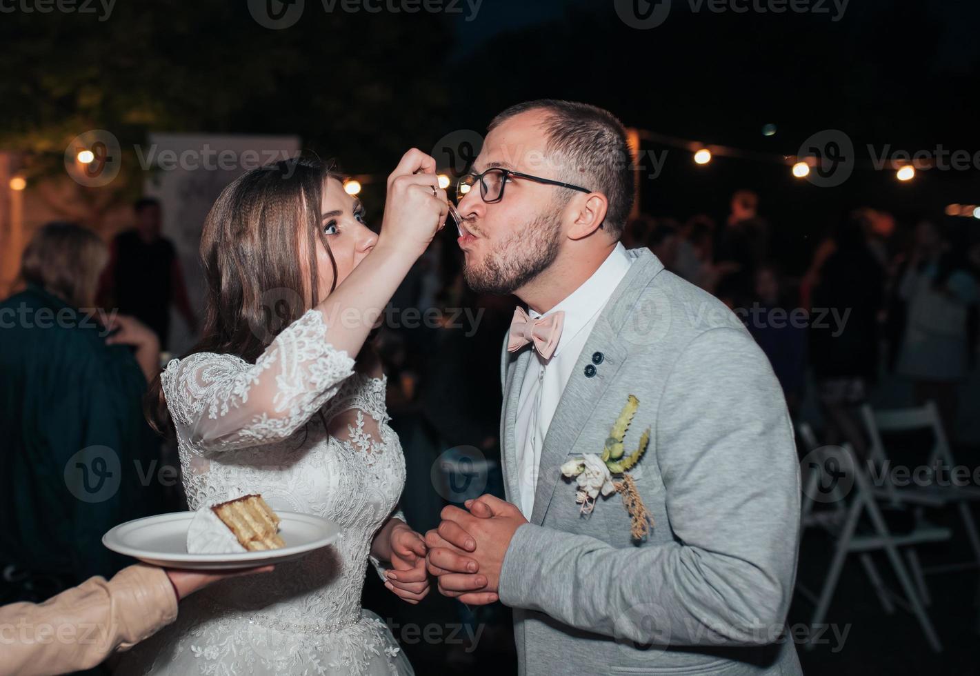 a noiva e o noivo na festa cortam e experimentam o bolo de casamento foto