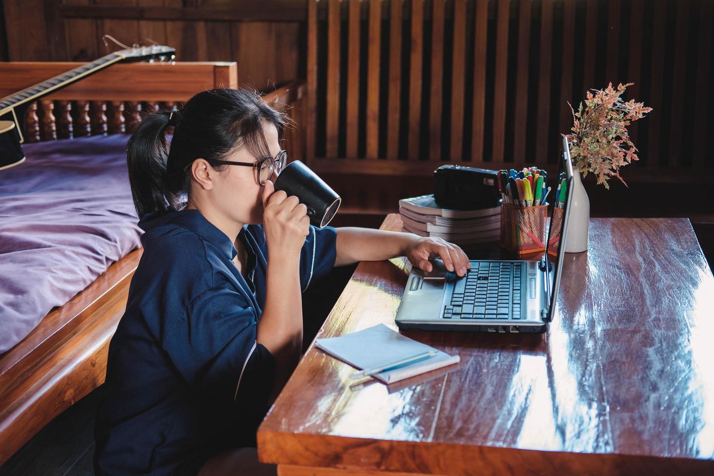 mulher tomando um café sentada no chão de casa escrevendo notas abertas no laptop na frente de seu conceito de escritório foto