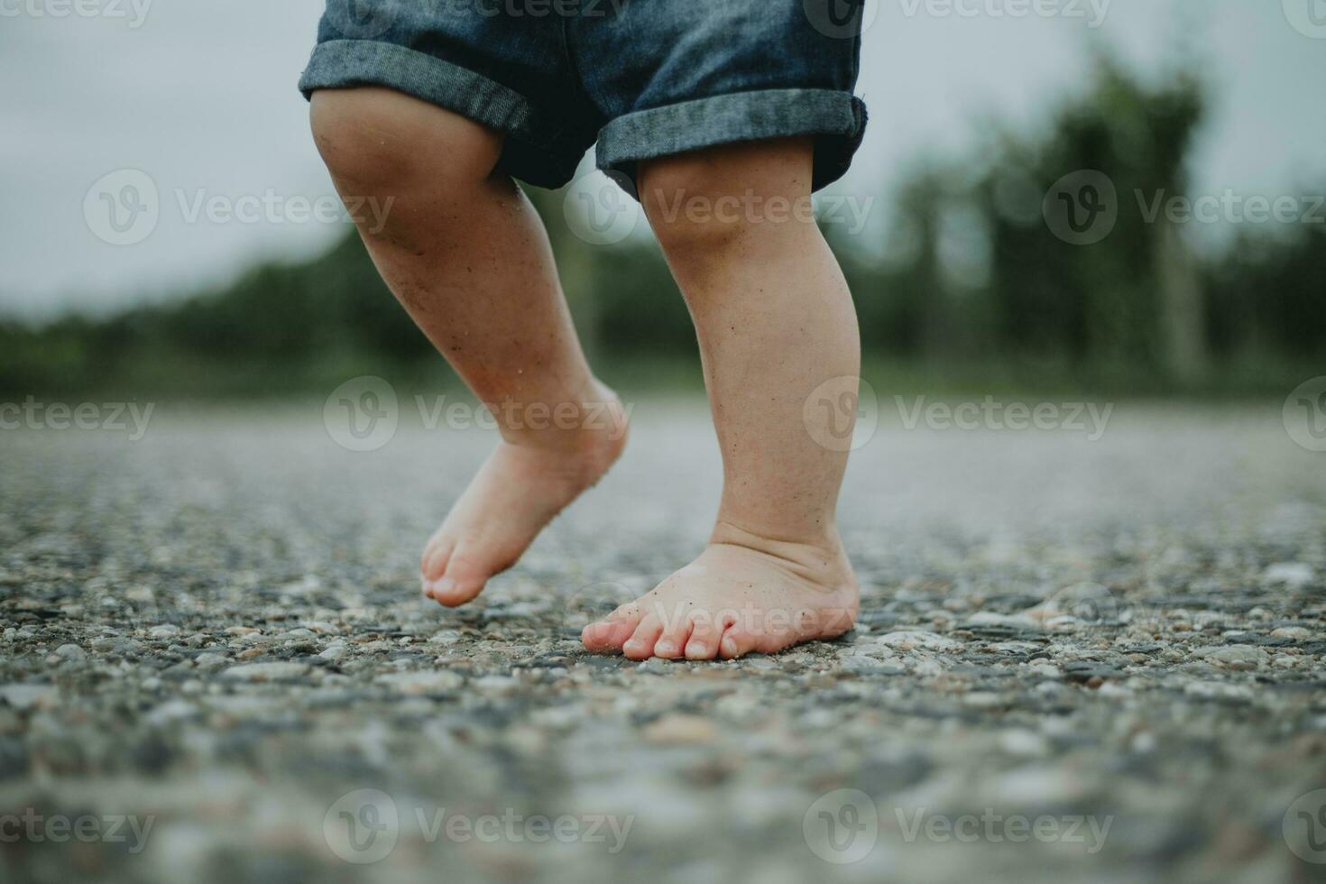 pequeno criança sujo pés pisar em a chão, vestindo jeans calção ocupado a partir de a baixo ângulo foto
