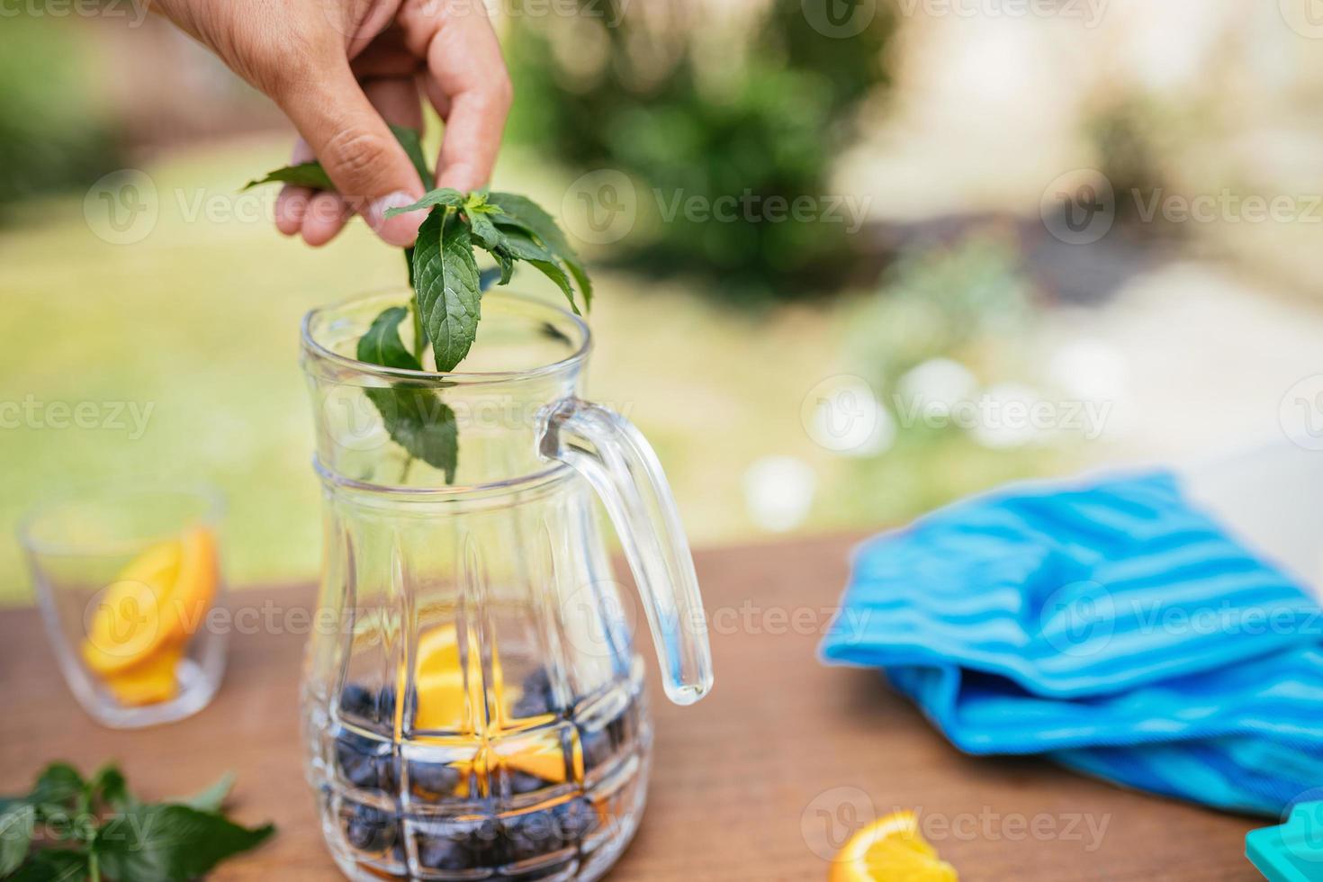 colocando hortelã na garrafa de vidro com mirtilos e laranja foto