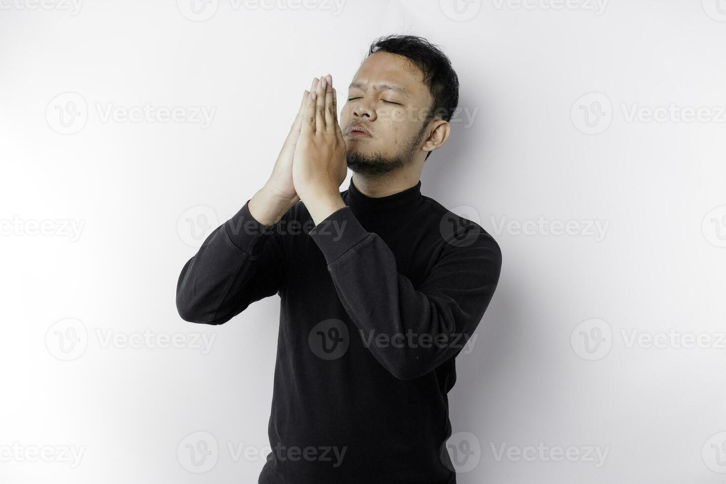 religioso ásia homem vestindo uma Preto camisa Rezar para Deus, isolado de uma branco fundo foto