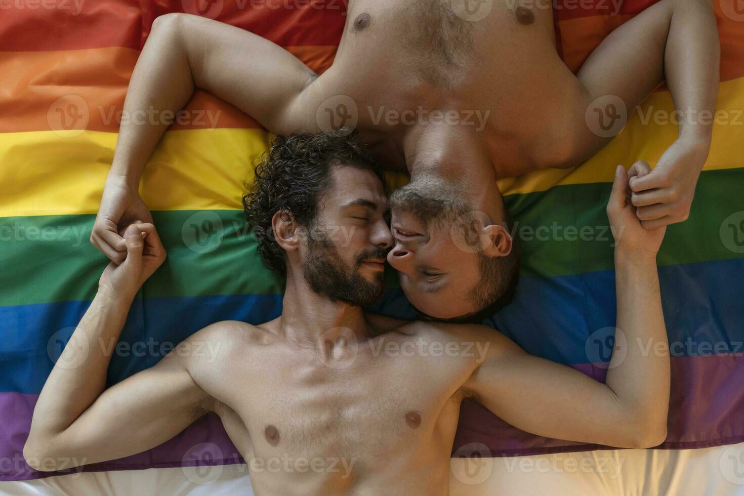 afetuoso jovem gay homem se beijando dele amante em a cama. dois jovem masculino amantes deitado juntos em orgulho bandeira. romântico jovem gay casal vínculo com carinho dentro de casa. foto