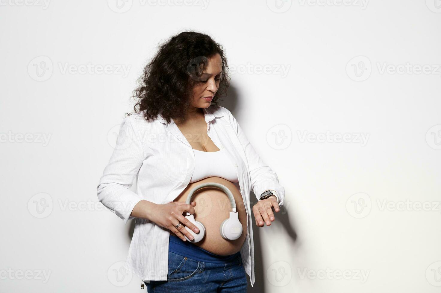 grávida mulher mãe colocação fone de ouvido em barriga, girando em música para dela futuro recém-nascido bebê isolado em branco fundo foto