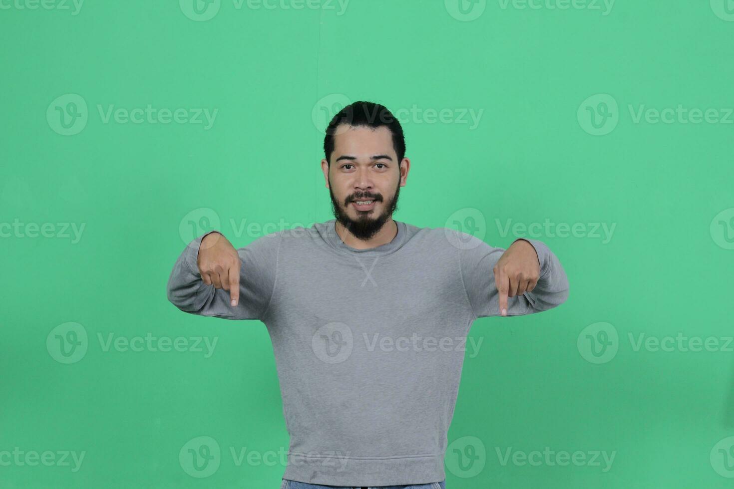 barbudo ásia homem poses vestindo uma cinzento camisa contra uma verde fundo foto