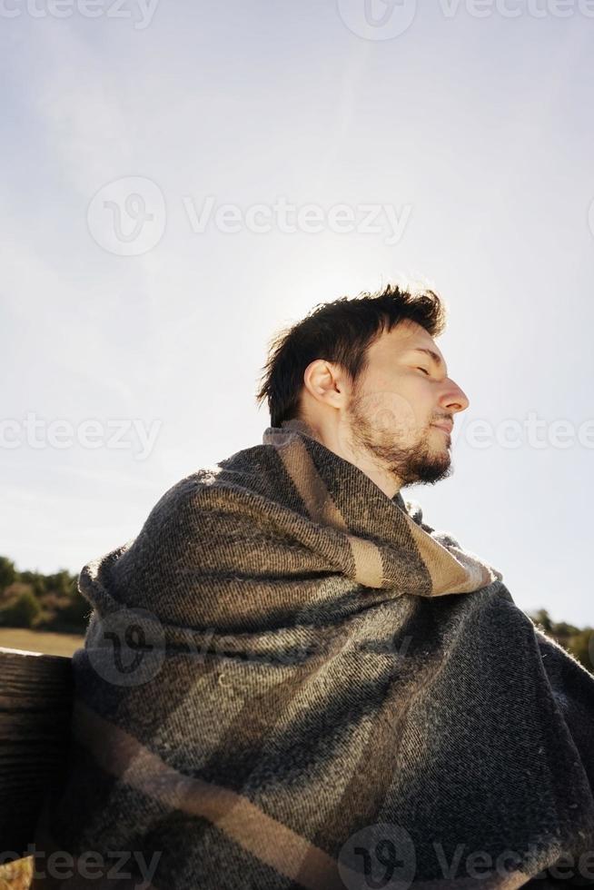 rosto lateral de um jovem de olhos fechados curtindo com calma o sol da manhã de outono com a luz de fundo do céu azul foto