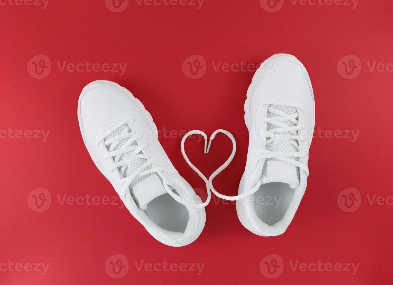 tênis esportivos brancos e cordões em forma de coração em um fundo vermelho. foto
