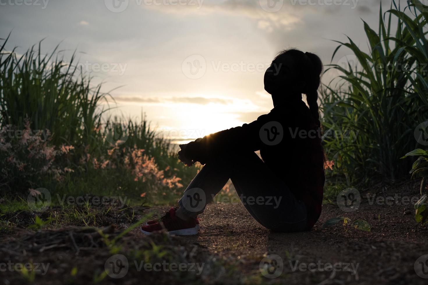 silhueta de mulher de agricultor sentada na plantação de cana-de-açúcar ao fundo, pôr do sol à noite foto