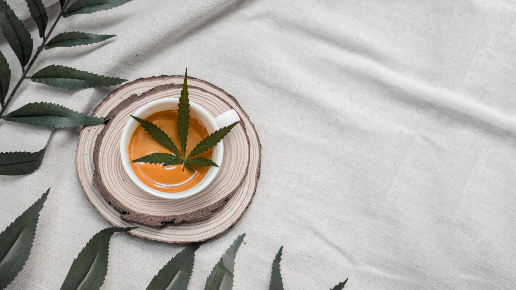 folha de cannabis em uma xícara de café em uma toalha de mesa branca foto