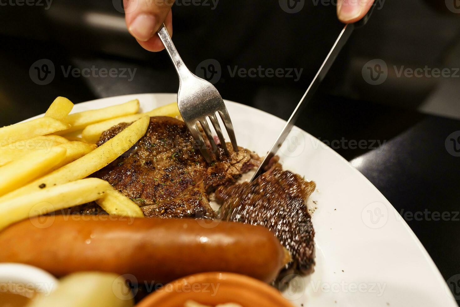 homem comendo grelhado carnes estaca a partir de placa. mão segurando faca e garfo corte grelhado carne bife foto