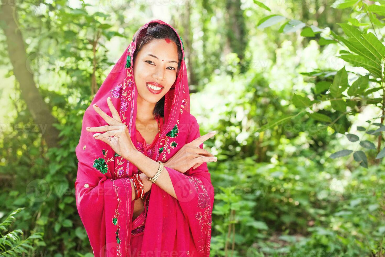 jovem lindo nepalês mulher vestindo saree em pé dentro uma natural fundo do floresta segurando dela mãos de dela face foto