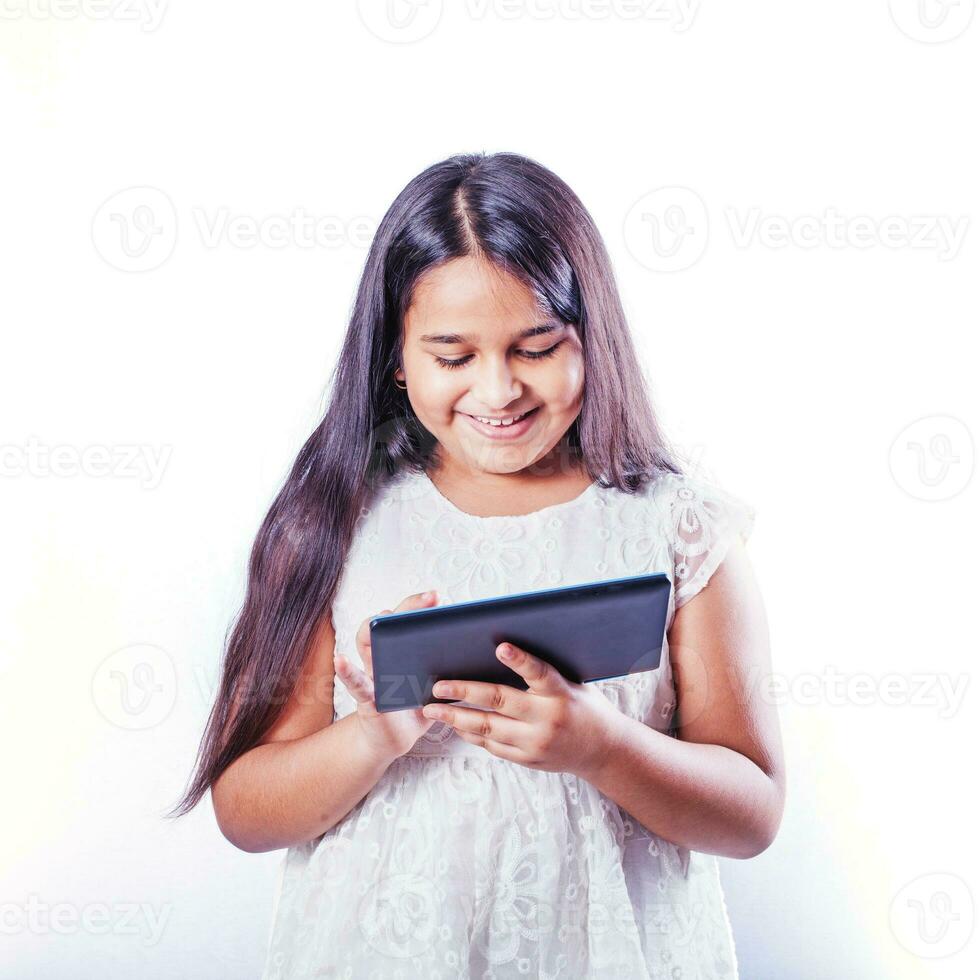 fofa indiano pequeno menina usando tábua computador em dela estúdio retrato em branco fundo foto