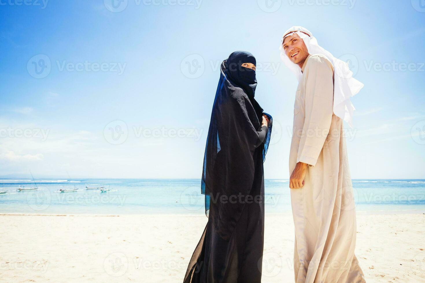 muçulmano casal em uma de praia vestindo tradicional vestir foto