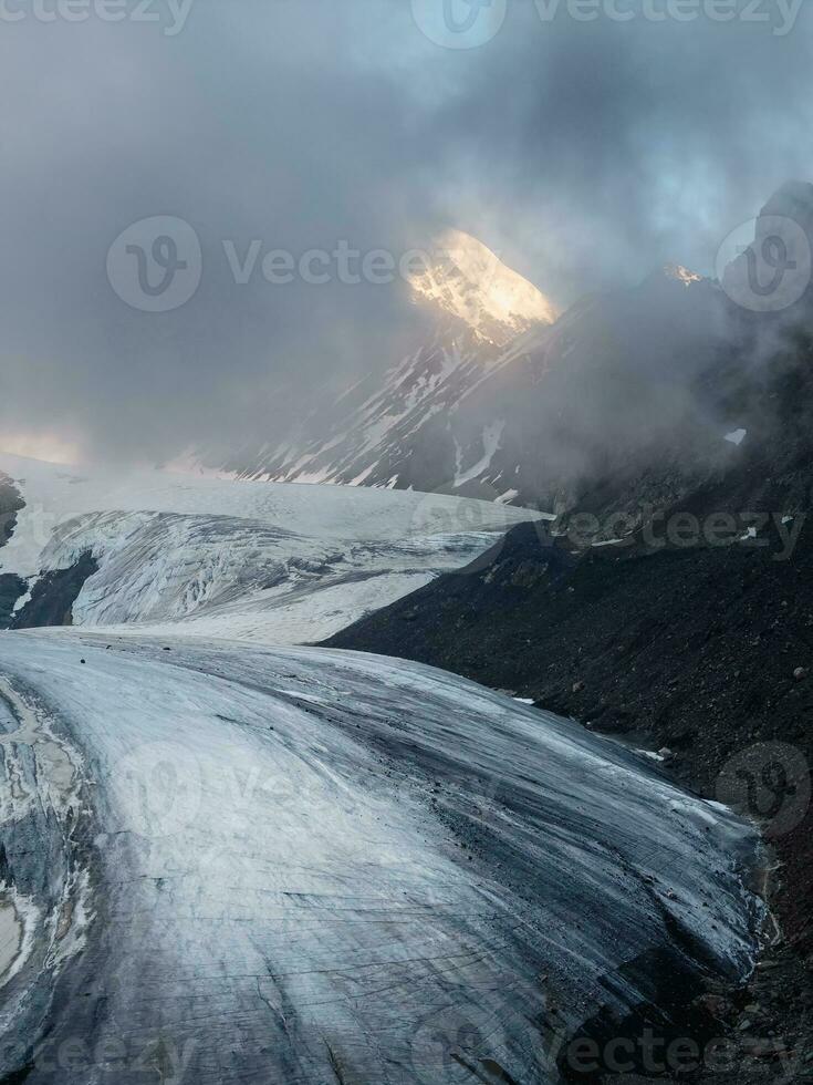 crepúsculo montanhas. luz em a geleira. majestoso geleira é iluminado de a brilhante dourado tarde Sol. vertical visualizar. grande aktru geleira, altai montanhas. foto