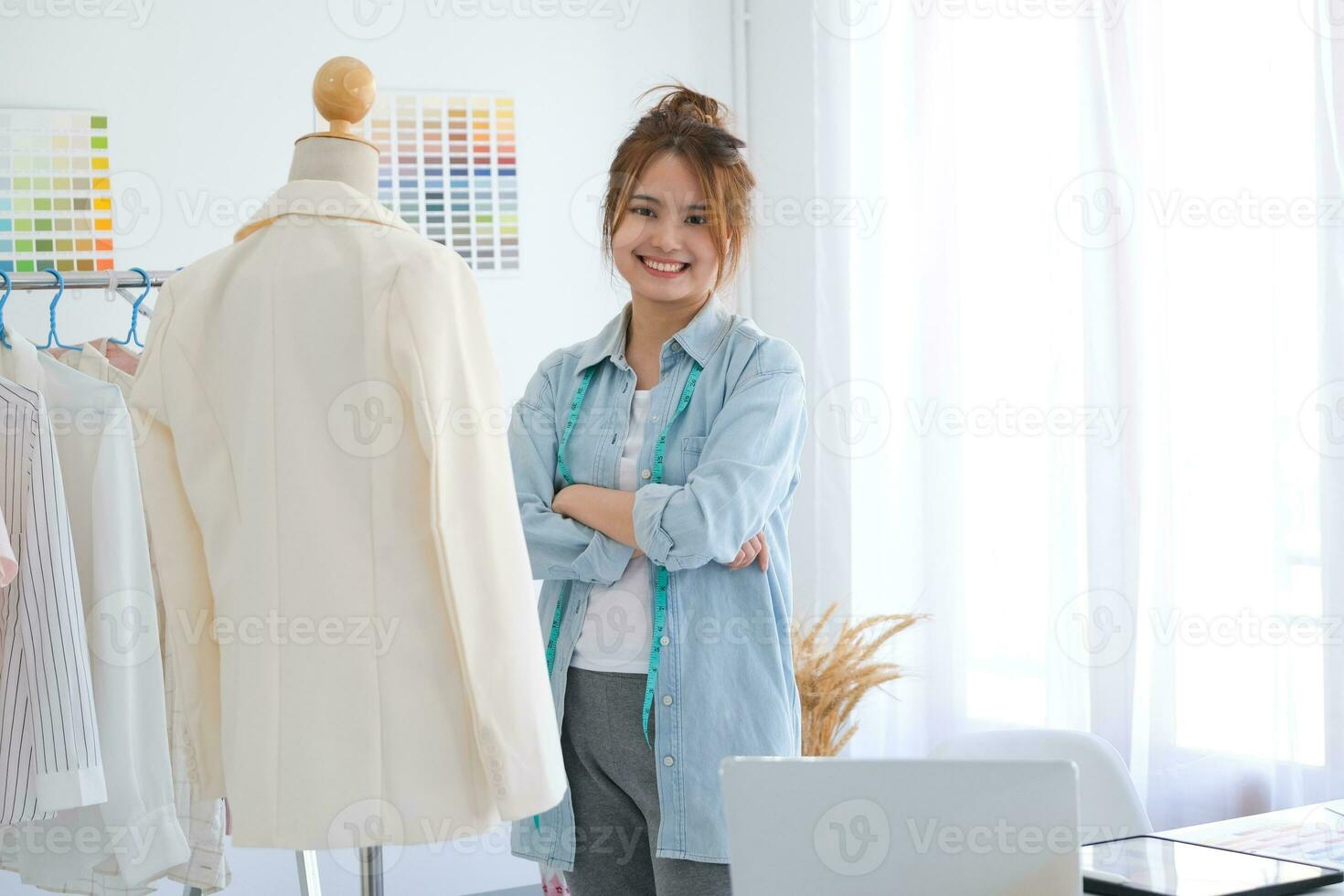 uma jovem ásia fêmea moda desenhador é em pé com braços guardada confiante e olhando às Câmera dentro dela Projeto estúdio. foto