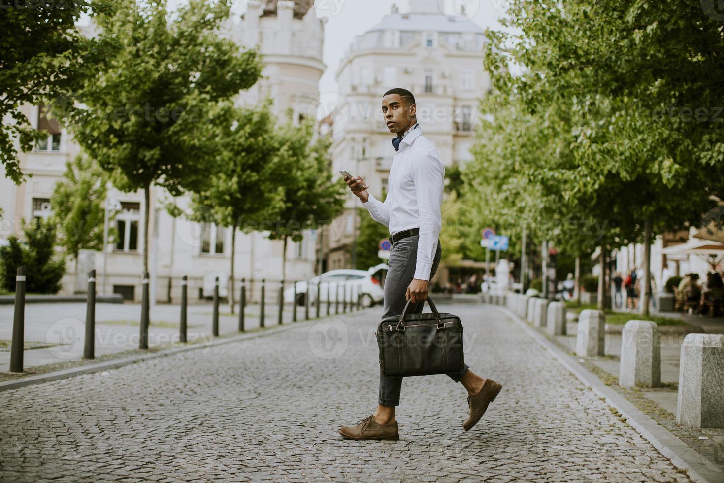 jovem empresário afro-americano usando um telefone celular ao atravessar uma rua foto