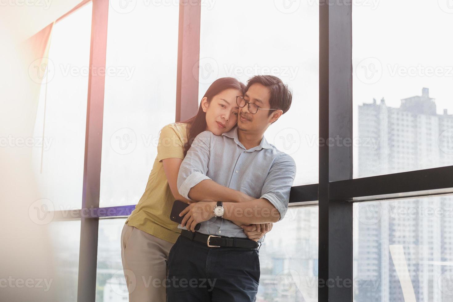 casal feliz se abraçando em pé ao lado de uma grande janela foto