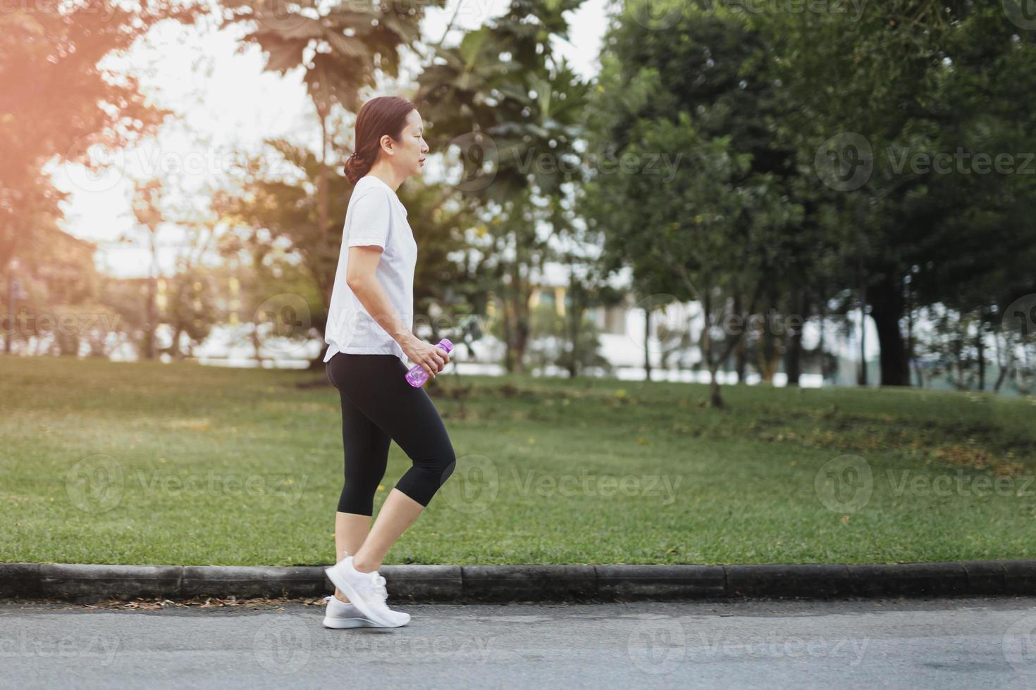 exercício de mulher caminhando no parque com a mão segurando uma garrafa de água foto