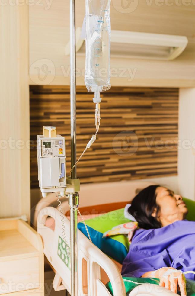 mão do paciente sênior com injeção de solução salina deitada na cama do hospital foto