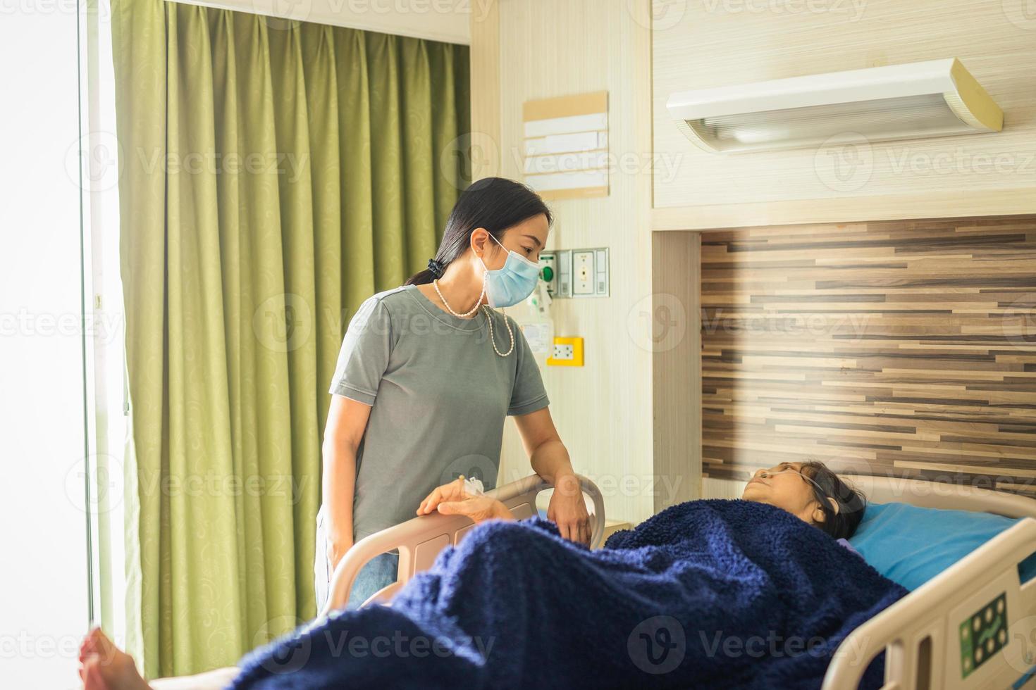 filha com máscara médica visitando a mãe deitada na cama na enfermaria do hospital foto