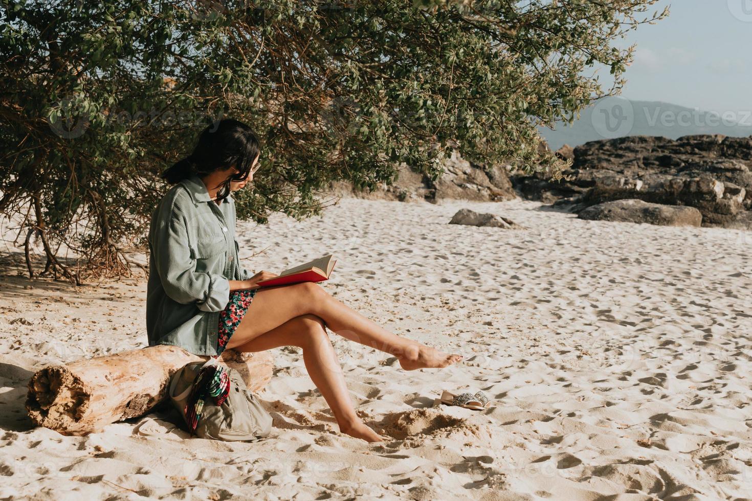 jovem marroquina com roupas modernas sentada na praia lendo um livro durante um dia ensolarado com espaço de cópia inspirador e tema de relaxamento com tons coloridos foto