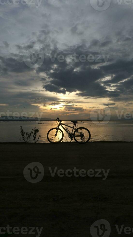 silhueta do uma bicicleta contra a fundo do a pôr do sol em a lago foto