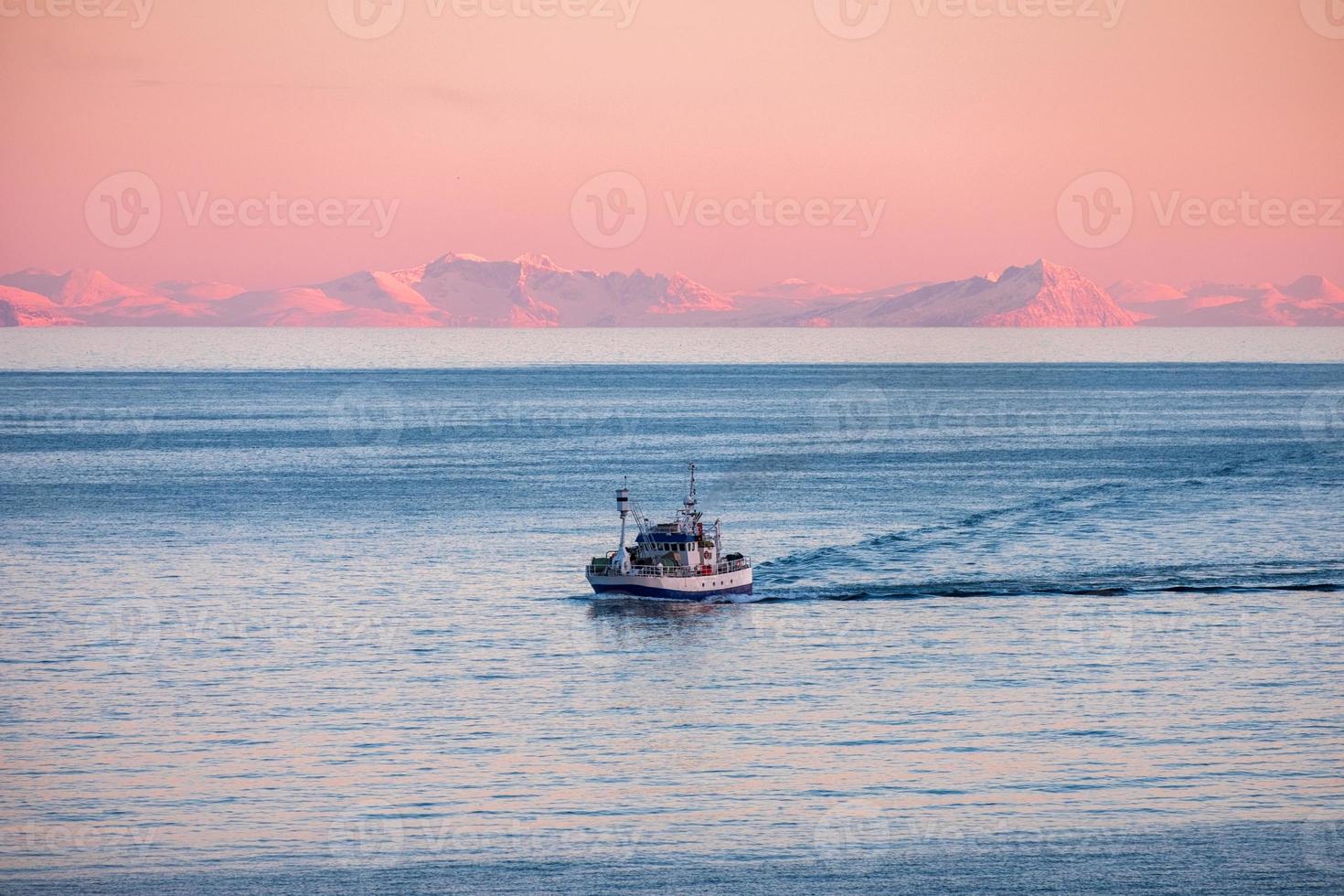 barco de pesca navegando pelo mar Ártico para pescar ao pôr do sol no inverno foto