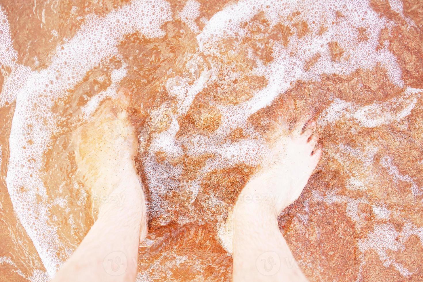 pés de homem na onda da praia foto