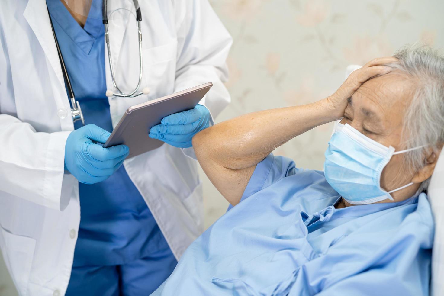 médico asiático usando protetor facial e terno novo normal para verificar paciente proteger segurança infecção covid 19 surto de coronavírus na enfermaria de quarentena do hospital foto