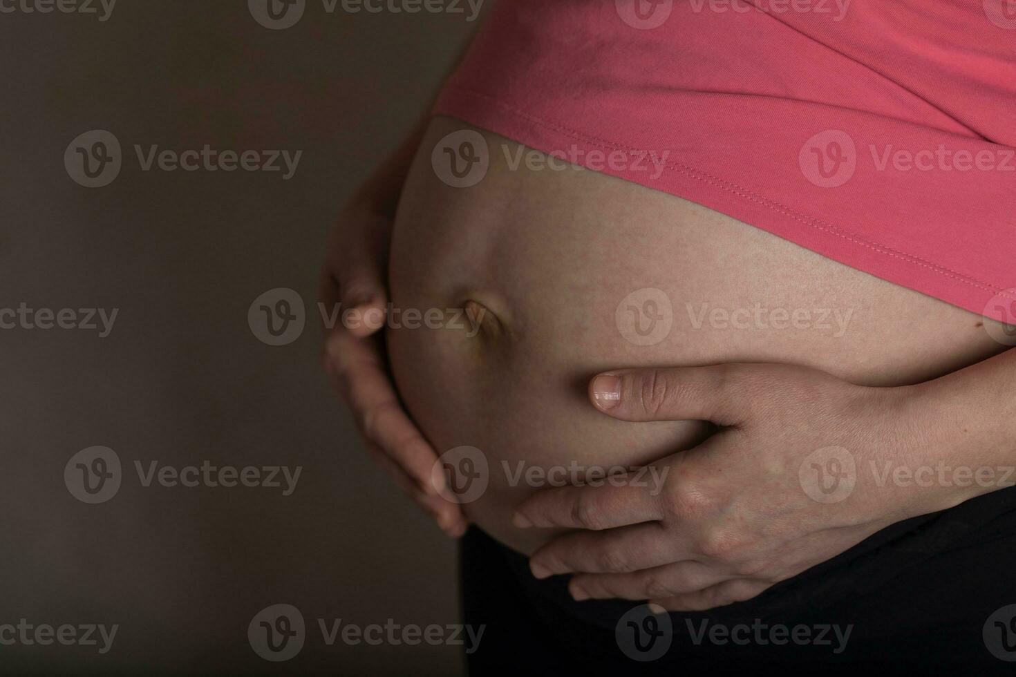 jovem grávida mulher toques dela barriga. dramático claro. foto