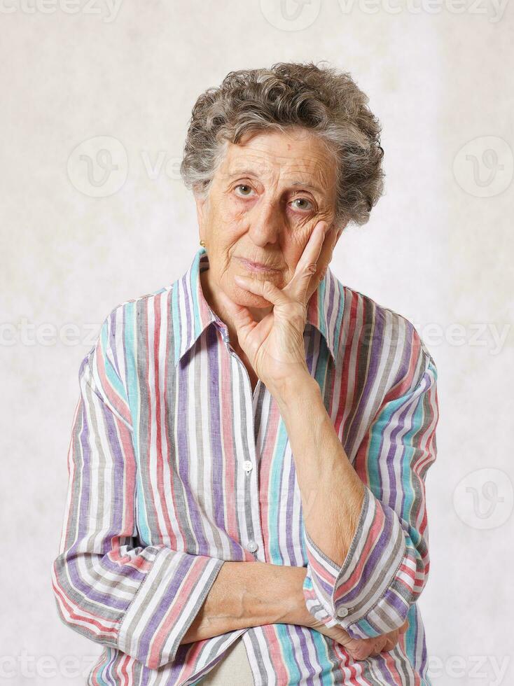 uma reflexivo Senior mulher. cinzento fundo foto