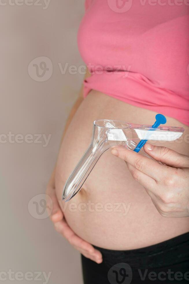 jovem grávida mulher mantém descartável vaginal espéculo fechar para dela barriga. foto