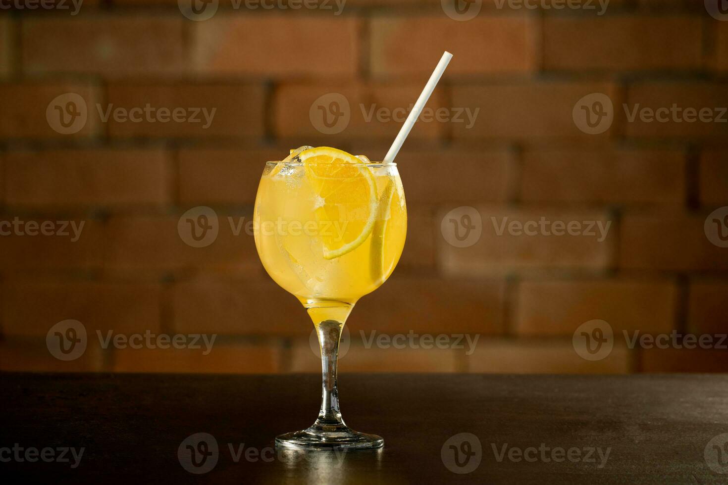 vidro do laranja Caipirinha beber em topo do mesa dentro frente do uma tijolo parede com texto espaço foto