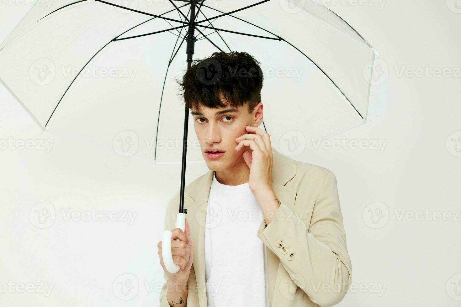 agradável jovem cara com a aberto guarda-chuva dentro uma terno luz fundo foto