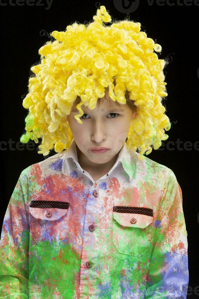 uma engraçado Garoto dentro uma amarelo palhaço peruca e colorida roupas com uma triste face. foto