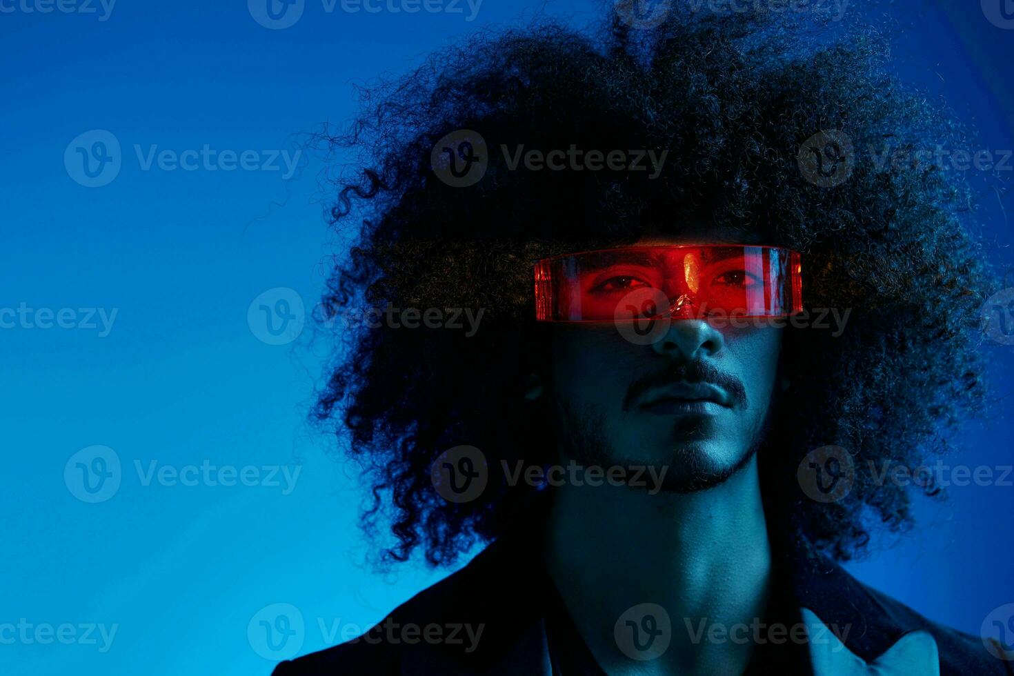 moda retrato do uma homem com encaracolado cabelo em uma azul fundo vestindo vermelho oculos de sol, multinacional, colori luz, na moda, moderno conceito. foto